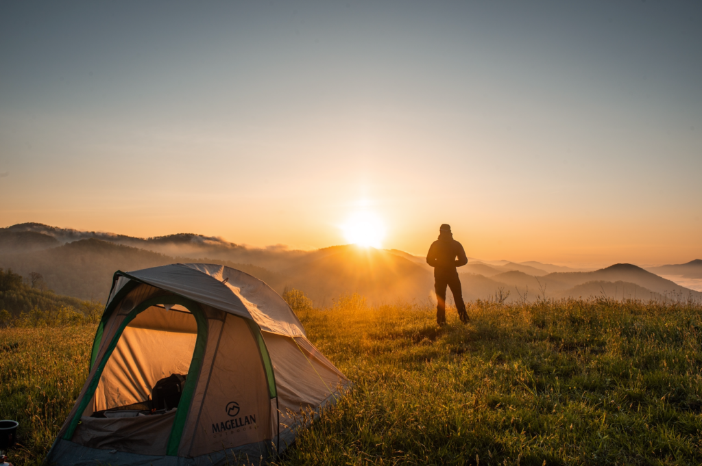An outdoorsman looks toward a sunrise near his Magellan tent